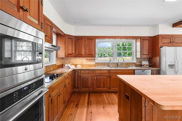 kitchen featuring stainless steel appliances, a sink, plenty of natural light, and brown cabinetry