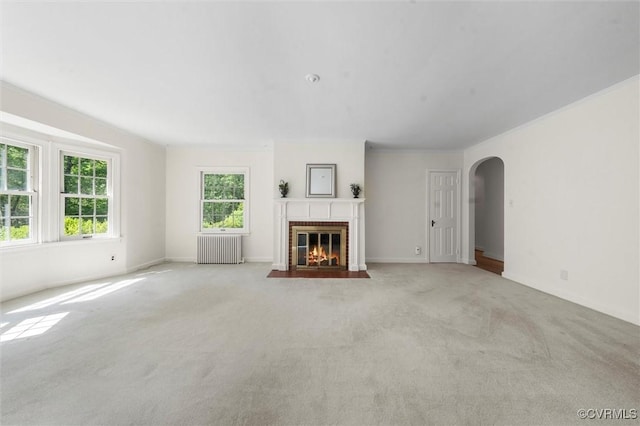unfurnished living room with radiator, arched walkways, carpet, and a fireplace with flush hearth