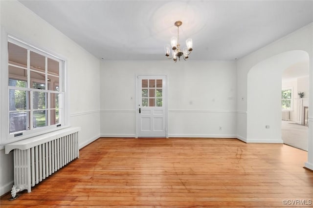 unfurnished dining area with radiator heating unit, light wood-style flooring, and a chandelier