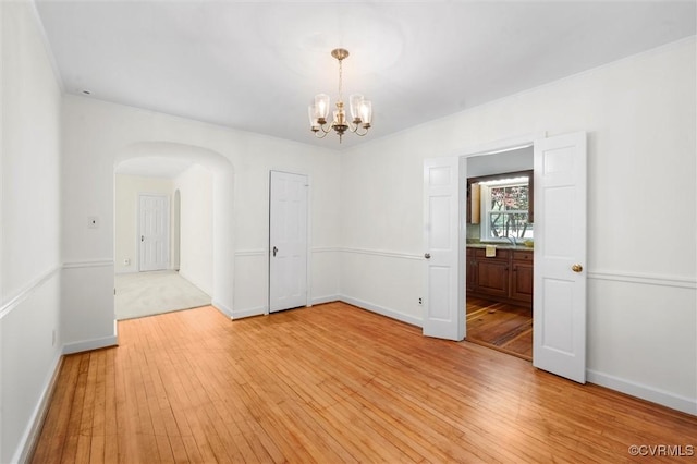 empty room featuring light wood-style floors, arched walkways, a chandelier, and baseboards