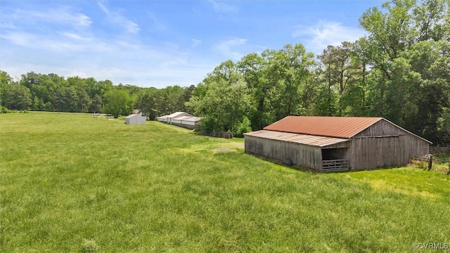 view of green lawn featuring an outdoor structure, a pole building, and a view of trees