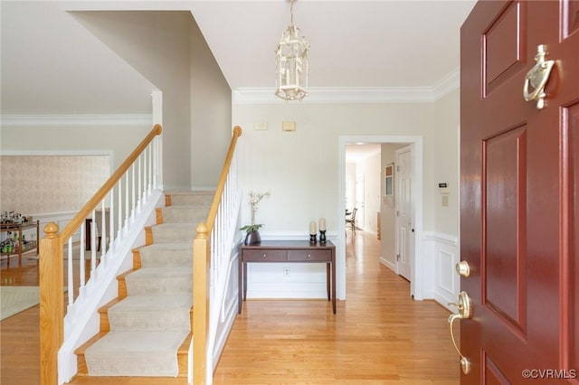 entryway featuring light wood finished floors, a notable chandelier, stairway, wainscoting, and ornamental molding