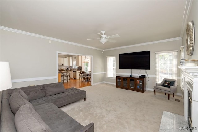 living area featuring light colored carpet, crown molding, baseboards, and a ceiling fan