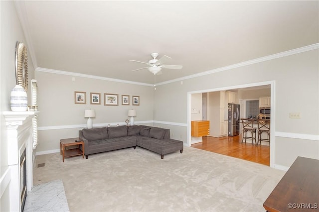 living area featuring crown molding, light carpet, a ceiling fan, and a fireplace with flush hearth