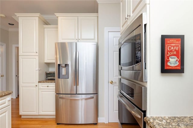 kitchen with light wood-style flooring, ornamental molding, light stone counters, white cabinetry, and stainless steel appliances