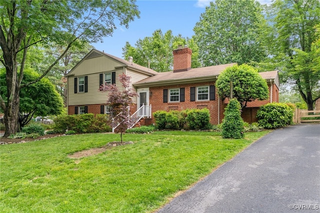 split level home with brick siding, a chimney, and a front yard