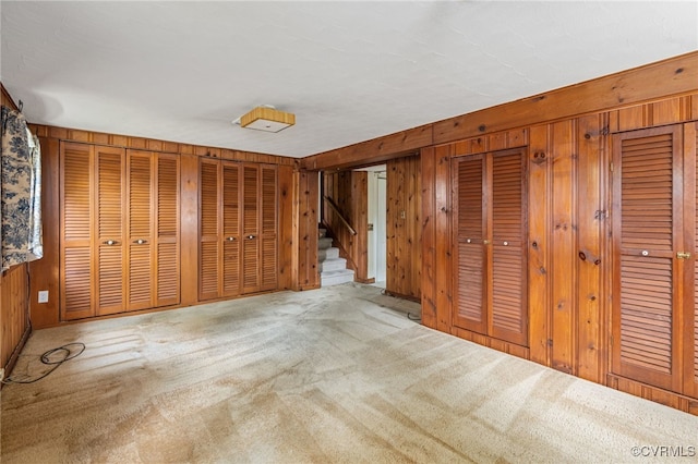 unfurnished bedroom featuring carpet floors, wooden walls, and two closets