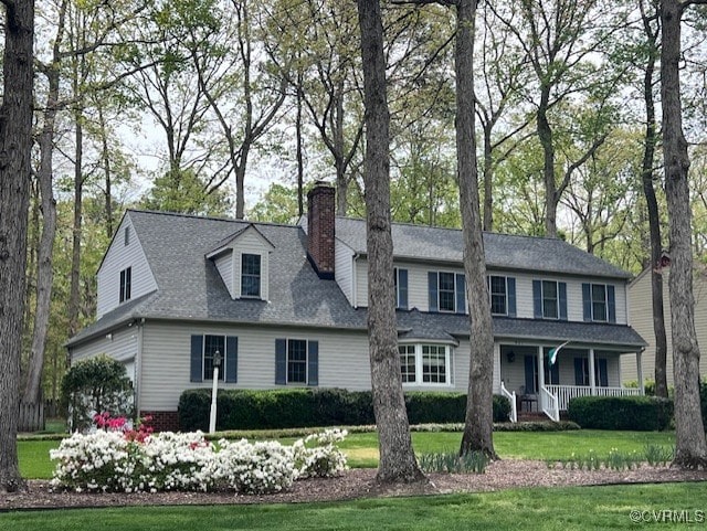 view of front of home with a porch, a chimney, a front yard, and roof with shingles