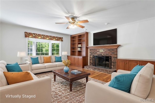 living room with wood finished floors, a ceiling fan, a fireplace, and crown molding