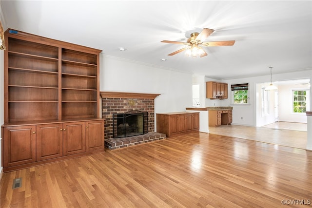 unfurnished living room with light wood-type flooring, ceiling fan, a brick fireplace, crown molding, and baseboards