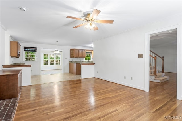 unfurnished living room featuring ornamental molding, a ceiling fan, light wood-style floors, stairway, and baseboards