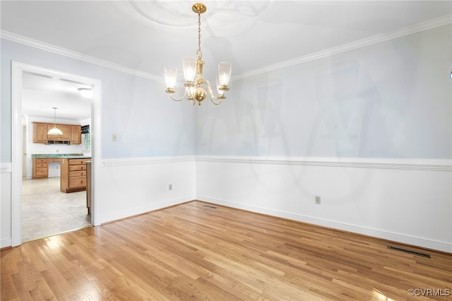 spare room with light wood-style flooring, a chandelier, and crown molding