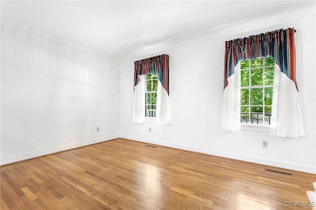 empty room with crown molding, healthy amount of natural light, wood finished floors, and baseboards