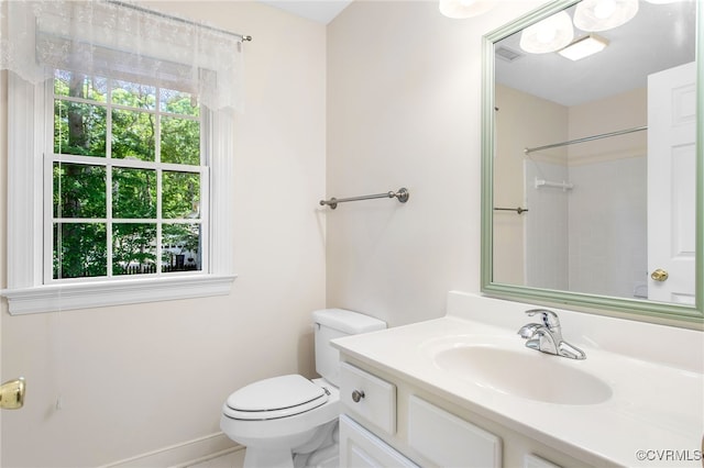 bathroom with toilet, vanity, baseboards, and a shower