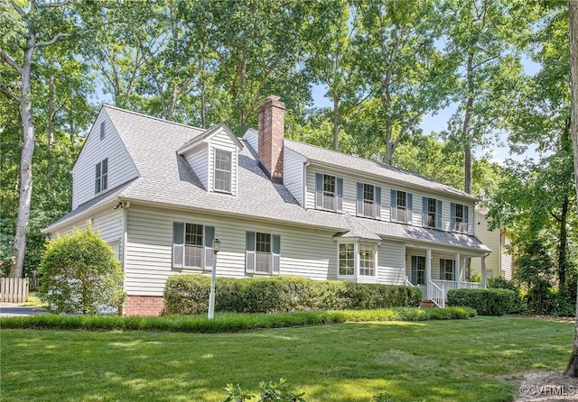 view of front facade featuring a chimney, a front lawn, covered porch, and a shingled roof