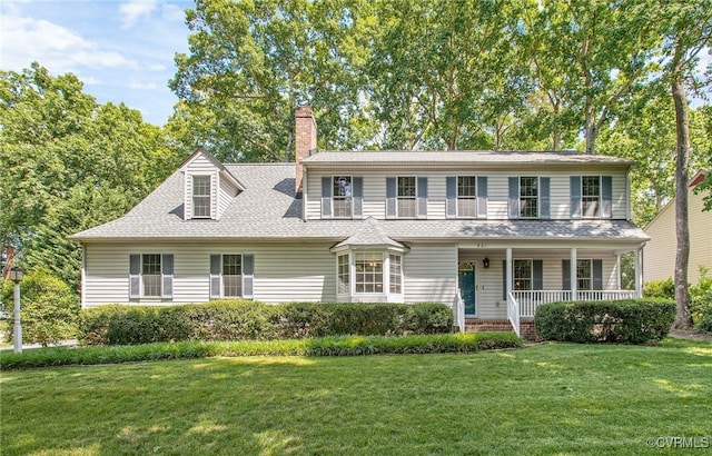 view of front of home with a chimney, covered porch, a front yard, and a shingled roof