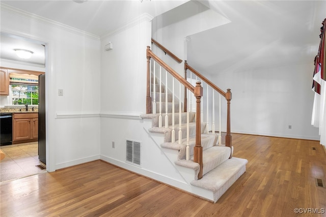 stairs with wood finished floors, baseboards, and crown molding