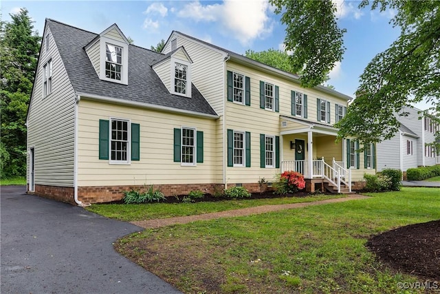 colonial house with driveway, covered porch, crawl space, roof with shingles, and a front lawn