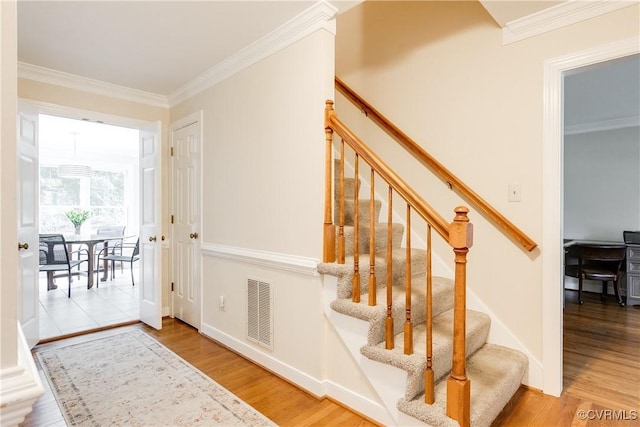 stairway featuring baseboards, crown molding, visible vents, and wood finished floors