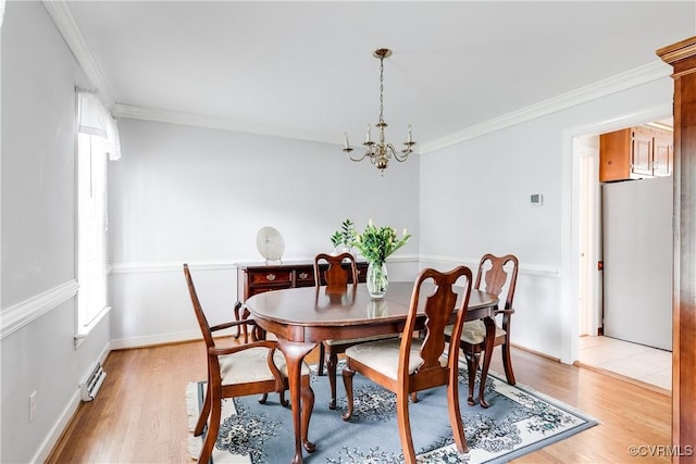 dining space featuring baseboards, light wood finished floors, a chandelier, and crown molding
