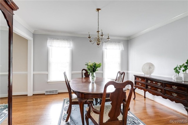 dining area featuring crown molding, a chandelier, light wood finished floors, and visible vents