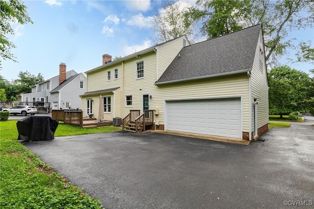 rear view of house with a chimney, driveway, a garage, a deck, and roof with shingles