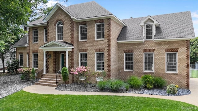 colonial home with roof with shingles, brick siding, and a front yard