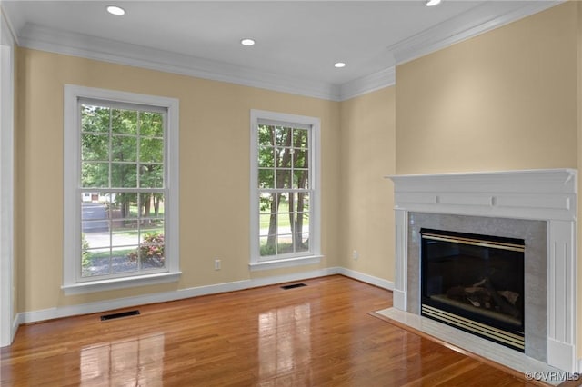 unfurnished living room featuring crown molding, a wealth of natural light, a high end fireplace, and wood finished floors