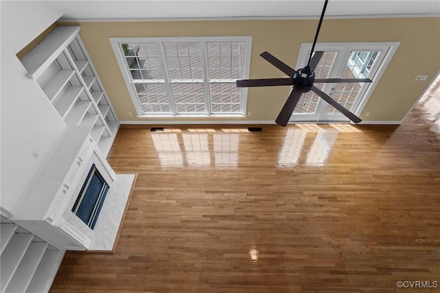 unfurnished living room with baseboards, ornamental molding, ceiling fan, a high end fireplace, and wood finished floors