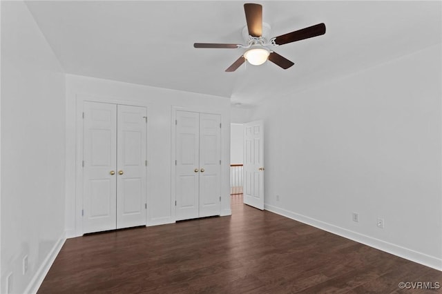 unfurnished bedroom featuring dark wood finished floors, baseboards, a ceiling fan, and multiple closets
