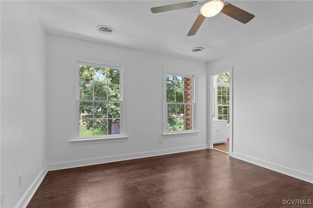 empty room featuring dark wood-style flooring, a wealth of natural light, and visible vents