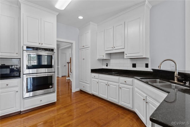 kitchen with light wood-style flooring, a sink, stainless steel double oven, white cabinets, and black microwave