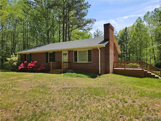 single story home featuring brick siding, a wooden deck, a chimney, and a front yard