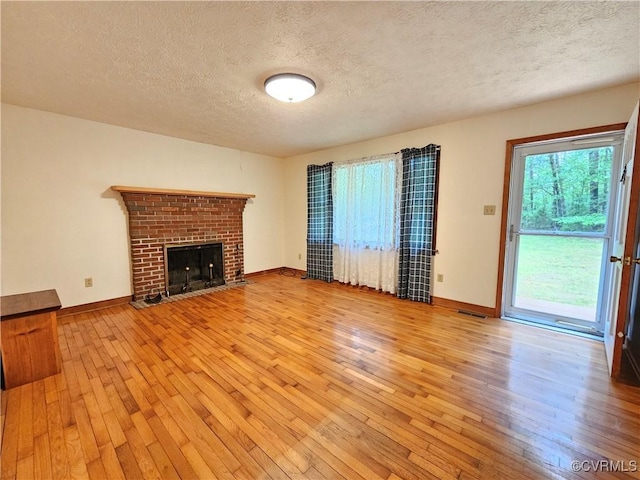 unfurnished living room with light wood finished floors, a textured ceiling, baseboards, and a brick fireplace