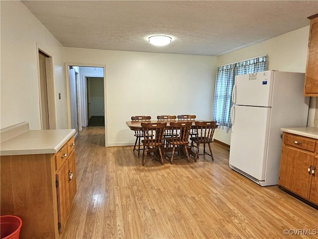 dining space featuring a textured ceiling, light wood-style flooring, and baseboards