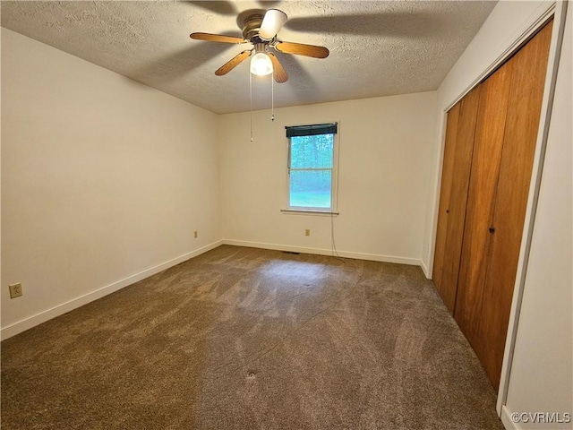unfurnished bedroom with a textured ceiling, dark colored carpet, a closet, and baseboards