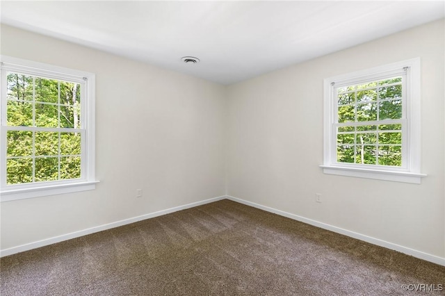 spare room featuring dark colored carpet, a wealth of natural light, and baseboards