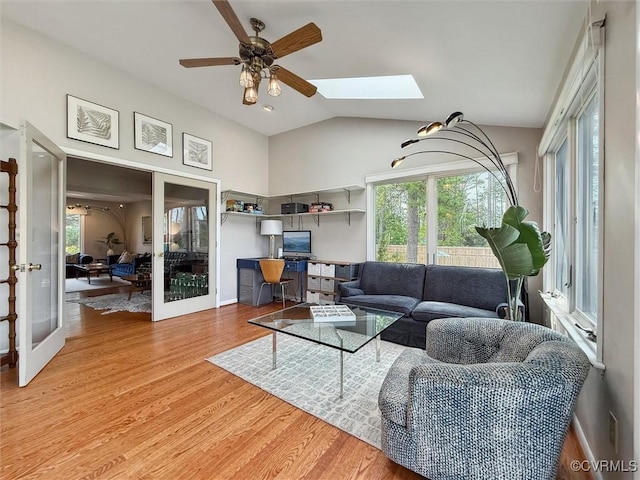 living area featuring lofted ceiling with skylight, baseboards, a ceiling fan, and light wood-style floors