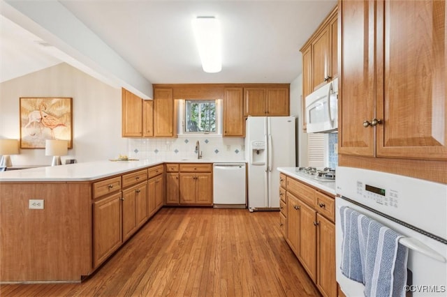 kitchen featuring light wood-style flooring, white appliances, a sink, a peninsula, and tasteful backsplash