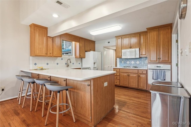 kitchen with white appliances, light wood finished floors, visible vents, a peninsula, and backsplash