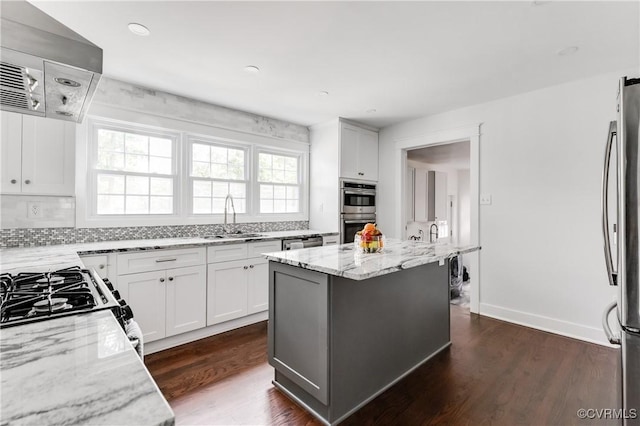 kitchen featuring a sink, exhaust hood, tasteful backsplash, light stone countertops, and appliances with stainless steel finishes