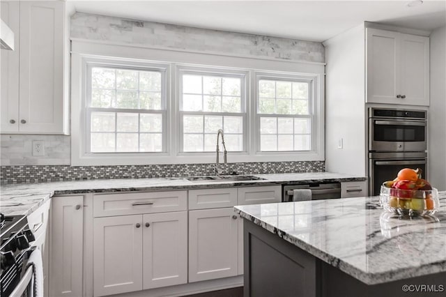 kitchen with backsplash, light stone counters, stainless steel appliances, and a sink
