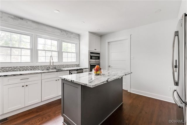 kitchen with a center island, a sink, stainless steel appliances, light stone counters, and dark wood-style floors