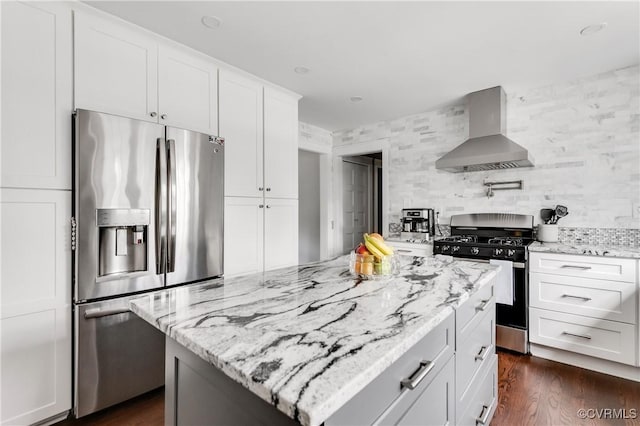 kitchen featuring wall chimney exhaust hood, white cabinets, light stone countertops, appliances with stainless steel finishes, and a kitchen island