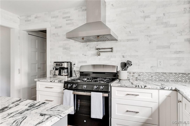 kitchen featuring stainless steel range with gas stovetop, white cabinetry, backsplash, wall chimney range hood, and light stone counters