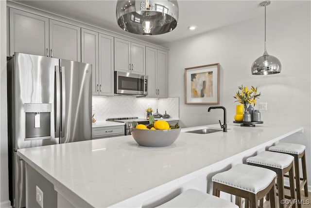 kitchen featuring gray cabinetry, a sink, a kitchen bar, decorative backsplash, and stainless steel appliances