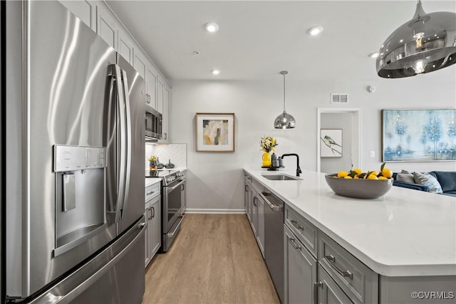 kitchen with a sink, a peninsula, gray cabinets, visible vents, and appliances with stainless steel finishes