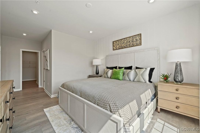 bedroom featuring light wood-style floors, baseboards, a spacious closet, and recessed lighting