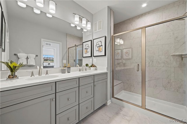 bathroom featuring a stall shower, marble finish floor, double vanity, and a sink