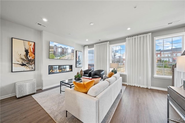 living room featuring baseboards, a glass covered fireplace, visible vents, and wood finished floors